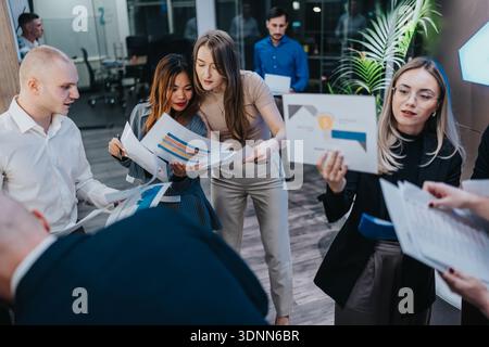 Team of diverse professionals collaborates in a modern office, reviewing charts and documents together during a brainstorming session Stock Photo