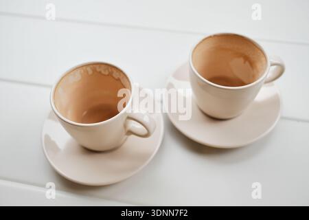 Two empty ceramic coffee cups on saucers standing on a white table after drinking coffee. Minimal lifestyle scene symbolizing pause, routine, and Stock Photo