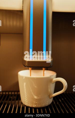 Fresh espresso pours from a coffee machine into a white ceramic cup. Flowing coffee creates a warm atmosphere and shows the brewing process in a Stock Photo