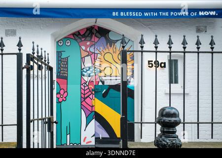 Colourful painted doorway behind an iron gate on Portobello Road, London, featuring street art and a mindfulness-themed banner. Stock Photo