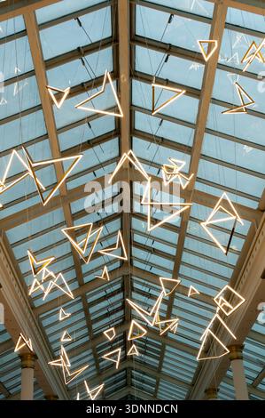 Symmetrical low angle view of triangular neon LED lamps suspended from a modern glass and steel vaulted ceiling. Concept of contemporary interior desi Stock Photo