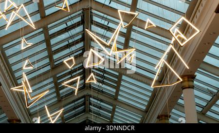 Symmetrical low angle view of triangular neon LED lamps suspended from a modern glass and steel vaulted ceiling. Concept of contemporary interior desi Stock Photo