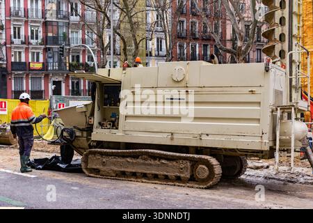 A heavy-duty tracked hydraulic rig stands on an asphalt street during a building renovation project. In the background, traditional apartment balconie Stock Photo