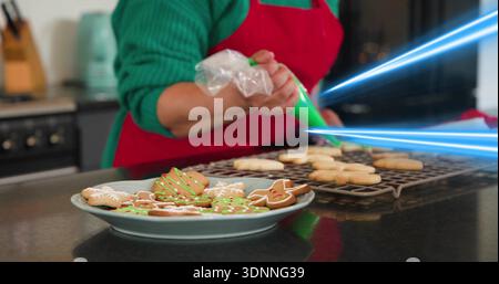 Decorating baker green sweater red apron piping cookies onto plate on home counter with piping bag Stock Photo