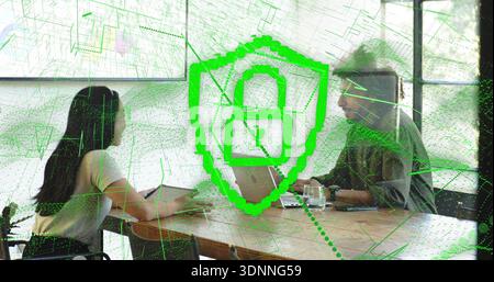 Discussing two colleagues in casual attire using tablet, laptop at meeting table, shield graphic Stock Photo