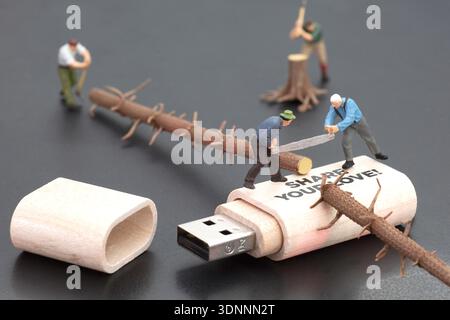 Miniature figures sawing wood on a USB flash drive illustrating manual labor and technology. Stock Photo