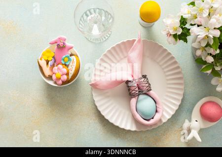 A vibrant Easter table setting features a beautifully arranged plate with a wrapped egg, decorated cookies, and fresh flowers, creating a joyful atmosphere for the holiday gathering. Stock Photo