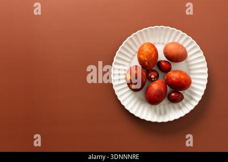 Vibrant Easter eggs in various shades of red and orange are beautifully arranged on a white plate, adding charm to the festive atmosphere of the season. Stock Photo