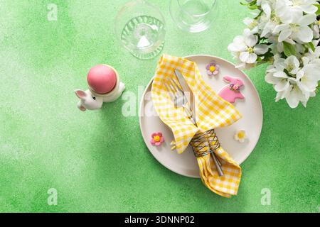 A vibrant Easter table setting features yellow checkered napkins wrapped with twine, a decorative plate, and fresh flowers, creating a festive atmosphere for spring gatherings. Stock Photo