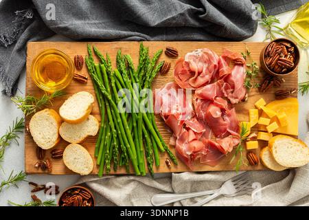 A beautifully arranged charcuterie board features fresh asparagus, various meats, cheeses, and nuts, set on a wooden plank with slices of bread. Perfect for sharing at gatherings. Stock Photo