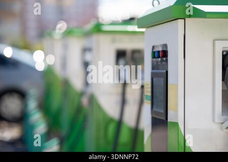 Close-up of an electric vehicle charging station with indicator lights and display. Row of EV chargers in the background with blurred car, modern gree Stock Photo
