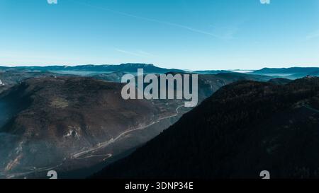 Aerial view from Mount Trebevic overlooking layered mountain ridges and winding roads near Sarajevo. Clear sky and vast horizons emphasize scale Stock Photo