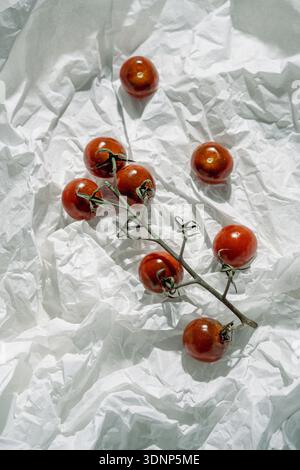 A cluster of ripe cherry tomatoes arranged artistically on crumpled white paper. The bright red tones contrast with the textured white background, hig Stock Photo