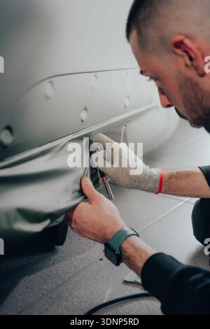 A skilled technician meticulously works on car wrapping, showcasing manual craftsmanship in auto customization at an automotive workshop. Professional Stock Photo