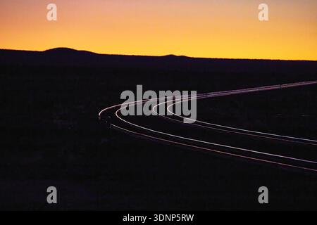 Golden Hour Train Tracks Curving Through Desert Landscape at Sunset Stock Photo