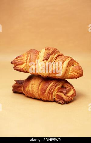 Two golden, flaky croissants are stacked on a light brown surface, capturing the essence of fresh, artisanal baking. Perfectly baked with a crisp exte Stock Photo
