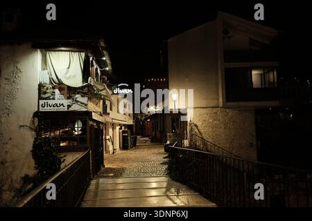 Narrow cobblestone street at night with restaurant signs and warm lantern light in the historic old town of Mostar. Mostar, Bosnia and Herzegovina - Stock Photo