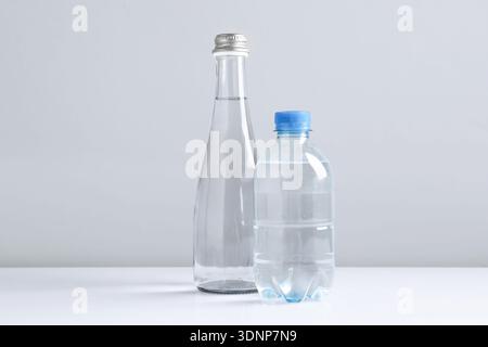 Water bottles of different sizes on white table against grey background Stock Photo