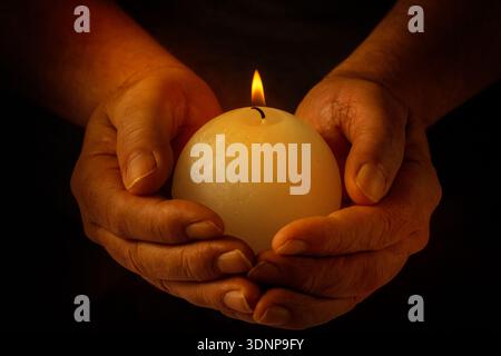 Male hands holding burning candle with flame on dark background Stock Photo