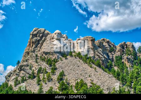 The mountain is covered in trees and has three large statues of men on it. The sky is blue and there are clouds in the background Stock Photo