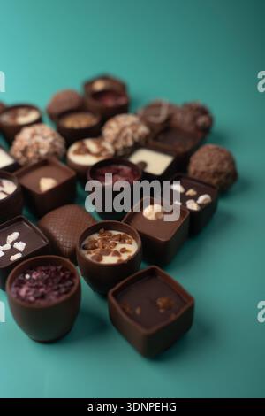 close-up of assorted artisanal chocolate bonbons and truffles arranged on a turquoise tabletop with shallow depth-of-field, glossy ganache, nut toppin Stock Photo