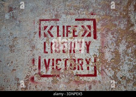 Graffiti Stencil on Weathered Concrete Wall with Urban Texture and Faded Red Paint Stock Photo