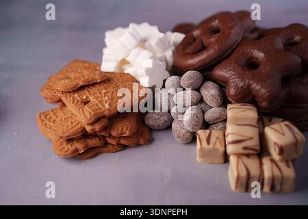 assortment of festive treats with spiced biscuits, chocolate-covered pretzels, sugary sweets, and decorated confections on a soft purple surface, gour Stock Photo