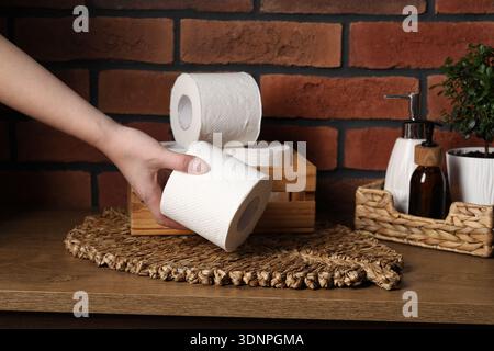 Woman taking toilet paper roll from box on wooden table, closeup Stock Photo