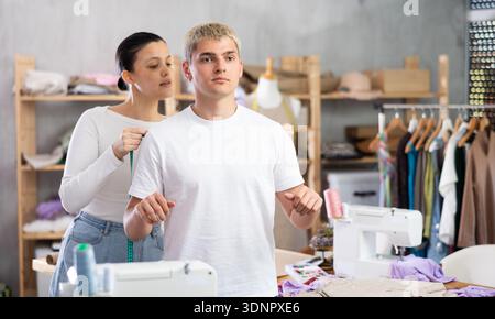 Professional young female fashion designer taking measurements of male client for sewing clothes in tailor shop Stock Photo