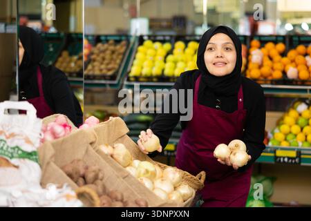 Muslim female seller in apron chooses quality onion Stock Photo
