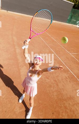 High angle view of tennis player serving ball with racket on outdoor clay court. Ideal for sports advertising, tournament promotion, and performance m Stock Photo