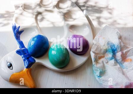 Top view of blue, green, and purple dyed easter eggs placed in molded egg holders on a decorative easter duck serving plate, Stock Photo
