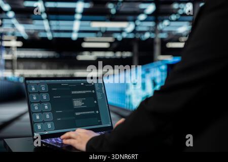 Close up of data center engineer using AI assistant on laptop to implement security measures, fortifying cyber threat defense. Server hub worker uses artificial intelligence LLM chatbot on notebook Stock Photo
