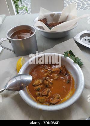 Mussels in broth served in white ceramic bowl surrounded by red chili ...