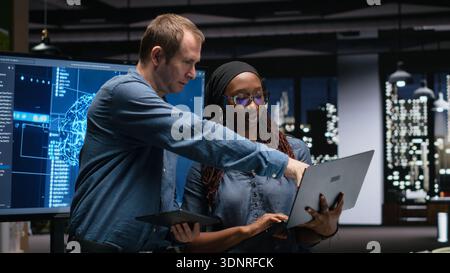 Technicians collaborating to develop artificial intelligence algorithms in high rise office late at night. Tech agency coworkers debug 3D neural network brain models Stock Photo