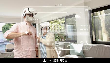 Selecting dates, senior couple wearing AR gear using holo calendar at home, woman in beige cardigan Stock Photo
