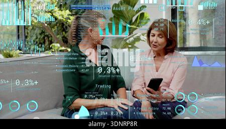 Reviewing two women in green and pink blouses checking black phone on patio sofa, HUD charts Stock Photo