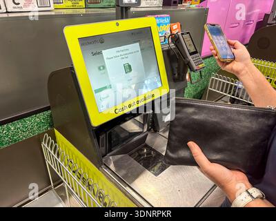Supermarket self check out terrminal,Woolworths supermarket in Sydney Australia, woman using her iphone to tap and pay for groceries, model released Stock Photo