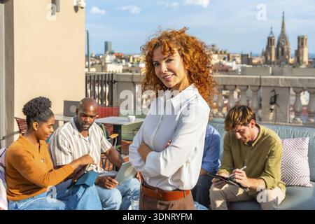 Team of diverse professionals working together on a city rooftop, engaging in discussions and tasks while experiencing a modern coworking environment Stock Photo
