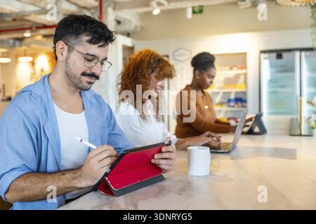 Diverse colleagues working on personal devices in a modern office, focusing on tasks and collaborating in a vibrant coworking space during a break or Stock Photo