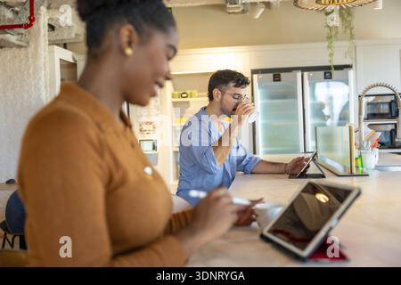 Coworkers are enjoying a coffee break in a modern co working space, using tablets for work or leisure, fostering a contemporary and flexible work envi Stock Photo