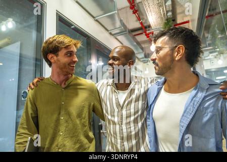 Diverse male colleagues walking together. Laughing and engaging in friendly conversation at a modern coworking office bringing together concepts of te Stock Photo