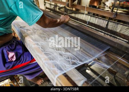 Close-up of a persons hands operating a loom, meticulously weaving a delicate, patterned fabric. Focus on the craft and detail. Stock Photo
