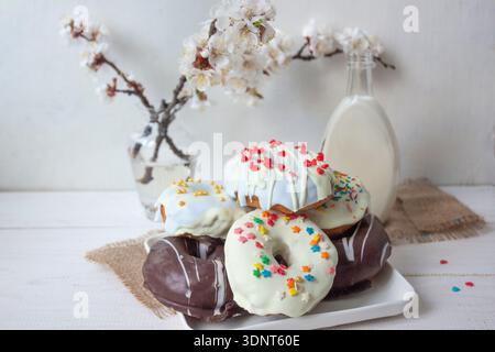 White Glazed Donut with Rainbow Sprinkles, Milk and Spring Blossoms Stock Photo