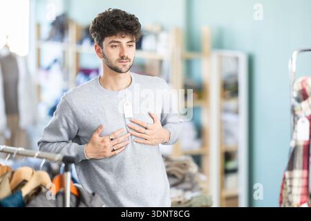 Young man trying on warm sweater in clothing store Stock Photo