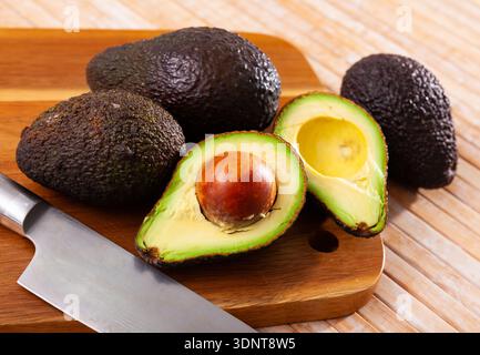Whole and sliced avocados on wooden board Stock Photo