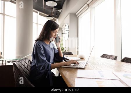 Young Asian businesswoman using cellphone and laptop for work communication Stock Photo