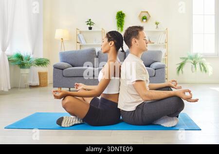 Couple meditating back to back at home on yoga mat in mindfulness together Stock Photo
