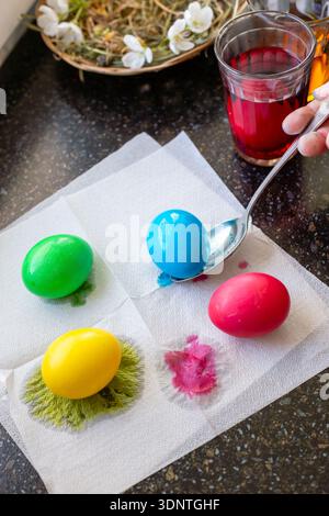 Brightly colored Easter eggs lie on white napkins with wet dye spots on a kitchen table. Holiday tradition, egg decorating, colorful celebration, East Stock Photo