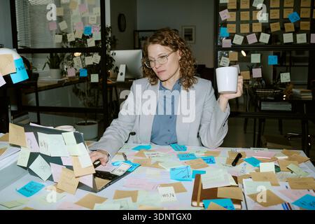 Young Adult Woman Working at Desk Surrounded by Sticky Notes Stock Photo